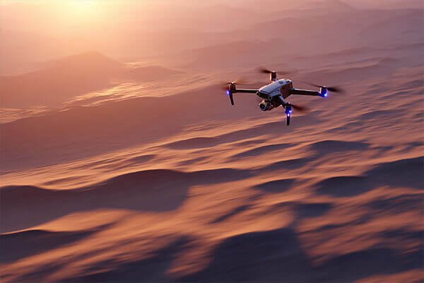 A drone flying confidently through a sandstorm in the desert and another flying in a snowy, arctic landscape.